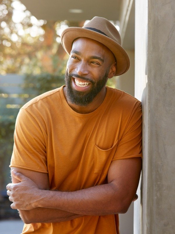 a happy and confident man wearing a hat smiles while looking into the distance