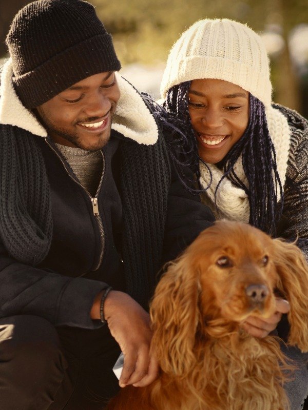 A happy couple in winter coats and hats plays with a dog