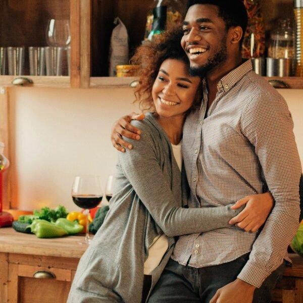 a smiling couple embraces in a kitchen during a party